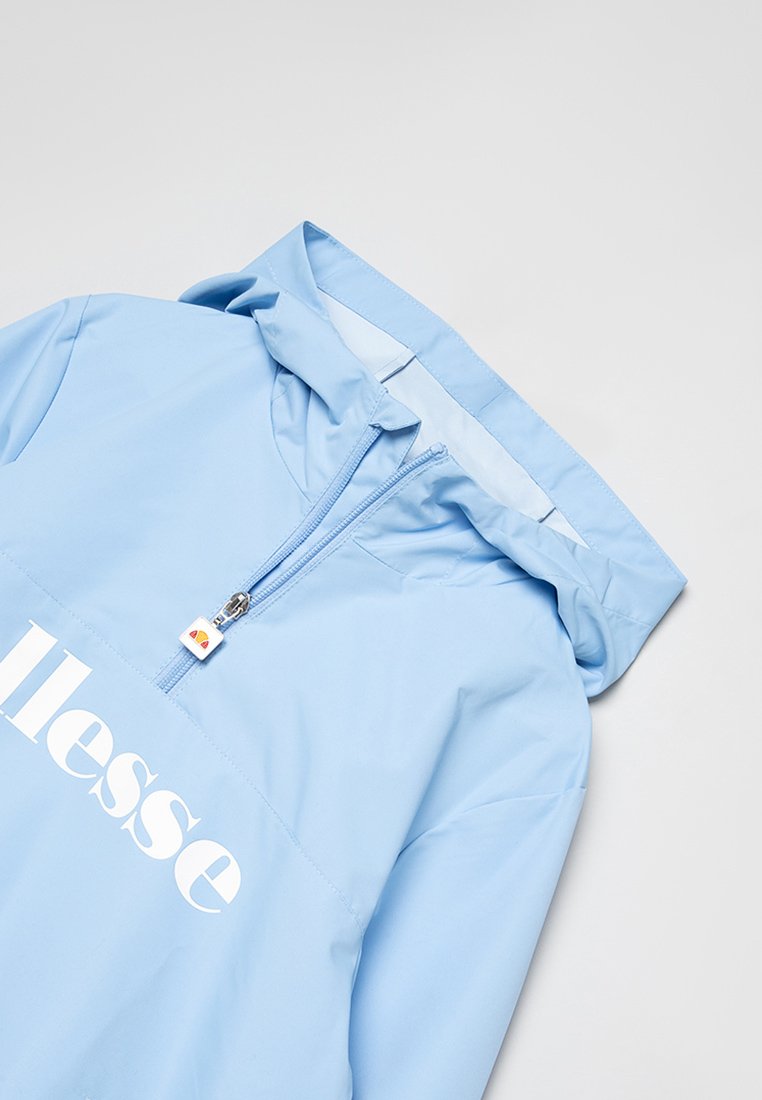 Chaqueta de sudadera azul claro con capucha, cierre de media cremallera y un logo blanco en el pecho. Tejido liso, resistente al agua y con un diseño sencillo.