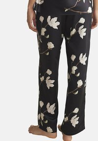 Pantalons de pyjama noirs avec un motif floral comprenant des fleurs de magnolia blanches et des feuilles vertes. Fabriqués en tissu lisse avec une coupe décontractée.
