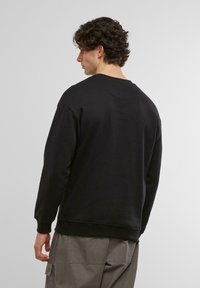 Sudadera negra de cuello redondo con puños y dobladillo acanalados, tela texturizada y un sutil detalle de costura en la parte posterior. Combinada con pantalones cargo grises.
