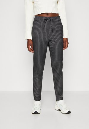Pantalons gris foncé à rayures, avec une taille à cordon de serrage, une coupe fuselée et une texture subtile, associés à des baskets blanches.