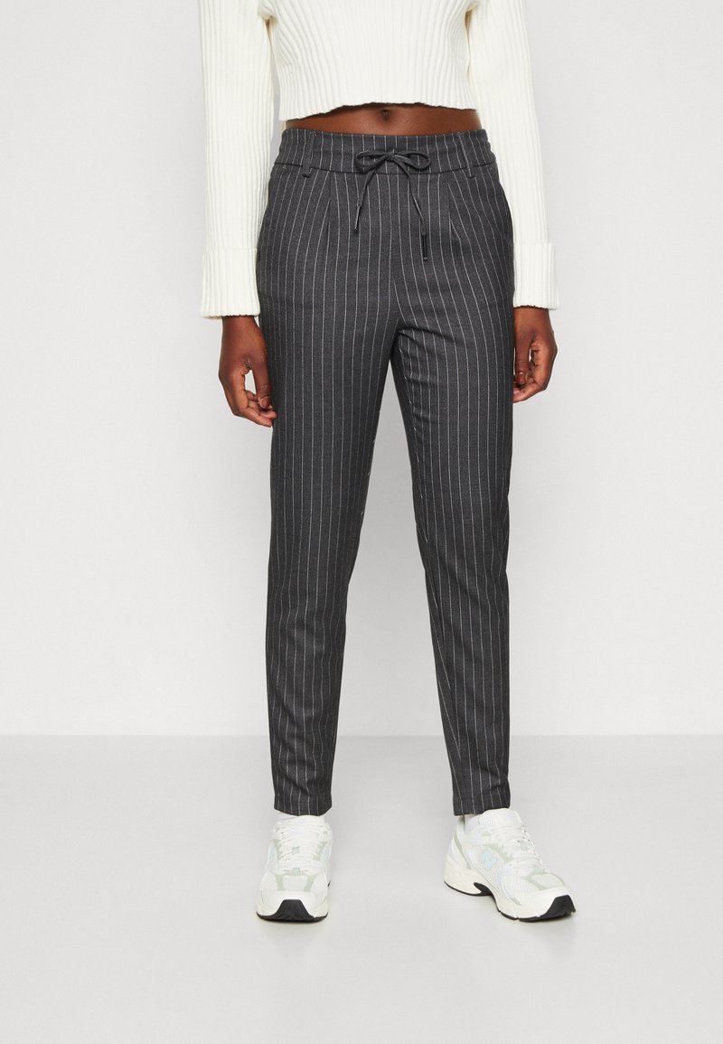 Pantalons gris foncé à rayures, avec une taille à cordon de serrage, une coupe fuselée et une texture subtile, associés à des baskets blanches.