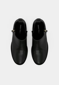 Crne gležnjače od glatke kože, s detaljem zlatnog metalnog patentnog zatvarača i zaobljenim vrhom.