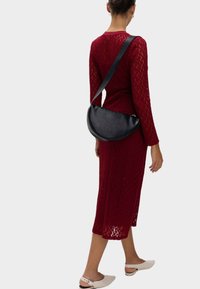 Rotes Spitzenstrickkleid mit langen Ärmeln, Länge bis zur Mitte der Wade, kombiniert mit einer schwarzen Leder-Umhängetasche in Halbmondform und weißen Slippern.