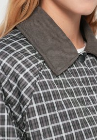 Μπουφάν με καπιτονέ σχέδιο σε αποχρώσεις του γκρι και μαύρου καρό, με υφασμένο γιακά από κορντούρο και μαύρο κούμπωμα με κουμπιά. Λείο, ελαφρύ ύφασμα.