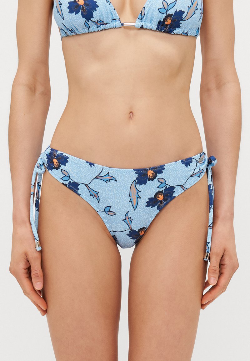 Šviesiai mėlynos spalvos bikini apatinė dalis su tamsiai mėlyna ir oranžine gėlių raštu. Šonai su reguliuojamais raiščiais, kad būtų galima pritaikyti kiekvienam individualiai.