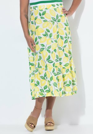 Kvinde iført en hvid midi nederdel med gult citron- og grønt bladprint, kombineret med brune plateau-sandaler.