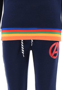 Marineblaue Hosen mit weißen Kordeln und rotem Avengers-Logo am linken Bein, kombiniert mit einem marineblauen Oberteil mit einem horizontalen Regenbogenstreifen am Saum.