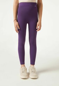 Paarse geribde leggings met een hoge taille, voorzien van een klein logo op de tailleband. Het model draagt beige gestructureerde sneakers.