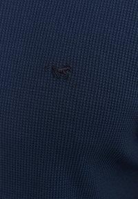 Navy blue ribbed knit shirt featuring an embroidered horse logo. Soft texture with a fitted design and subtle pattern.