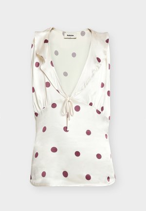 Top en satin crème sans manches avec des pois mauves, col en V profond, détail volanté aux épaules, et fermeture à nouer devant.