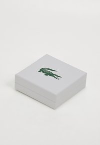 Scatola quadrata bianca con superficie testurizzata, caratterizzata da un logo di coccodrillo verde sulla parte superiore. Il design è minimalista e pulito.