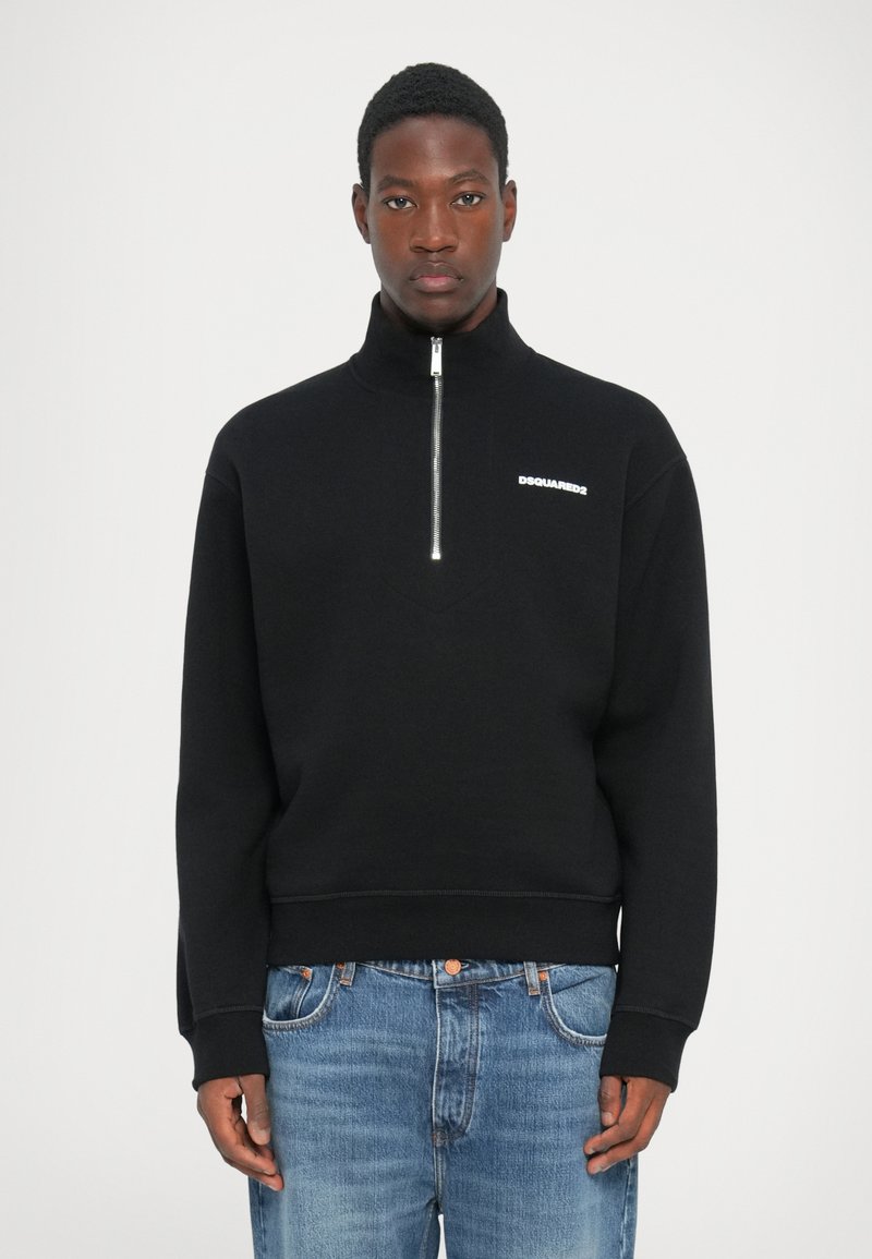 Zwarte zip-up sweatshirt met een hoge kraag, voorzien van een wit logo op de borst. Draagt bij blauwe denim jeans, die een relaxte pasvorm laten zien.