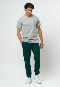 Grå bomulls T-shirt med rund halsringning och liten logotyp, ihop med gröna sweatpants med elastiska muddar och vita sneakers.