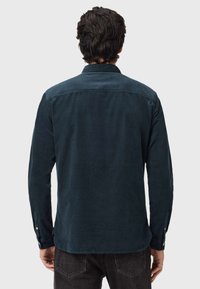 Camicia incorduroy blu navy con maniche lunghe, polsini con bottoni e dettagli sul dietro, caratterizzata da una texture morbida e una vestibilità su misura.