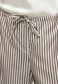 Λεπτομέρεια μέσης καφέ και λευκών κάθετα ριγέ παντελονιών με υφασμάτινη ζώνη δεμένη σε φιόγκο στο κέντρο μπροστά.