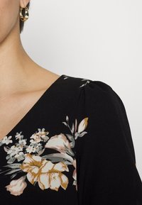 Vestido preto com estampado floral e decote em V. Apresenta padrões de flores em rosa claro, amarelo e verde. Tecido texturizado com detalhe de ombros bufantes.