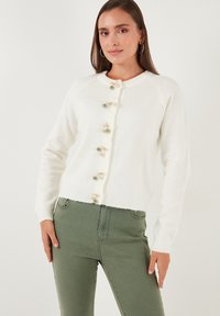 Cardigan blanco de mezcla de lana con cuello redondo, dobladillo acanalado y botones decorativos con pequeños acentos en verde y dorado. Mangas largas, estilo ajustado.