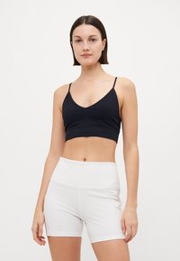 Black ribbed crop top with thin straps, paired with high-waisted white shorts. Both have a smooth texture and a fitted design.