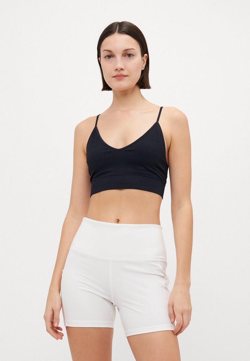 Black ribbed crop top with thin straps, paired with high-waisted white shorts. Both have a smooth texture and a fitted design.