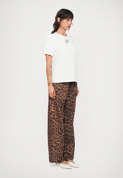 Valge lühikeste varrukatega t-särk väikese graafikaga rinnus, kombineeritud laia jalaga leopardimustriliste pükstega pruunis ja mustas.