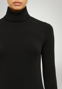 Svart polotröja i elastiskt tyg, med långa ärmar och en tajt design med en slät, matt yta.