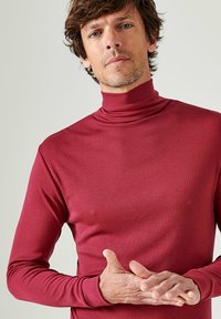 Maglietta a maniche lunghe con colletto alto di colore borgogna, realizzata in un tessuto morbido ed elasticizzato. Design aderente con colletto alto e dettagli minimi.