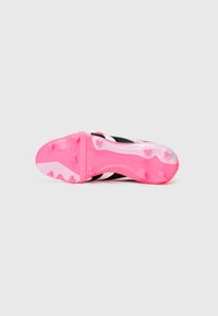 Chuteira de futebol preta e branca com uma sola texturizada rosa, apresentando cravos curvos e "PREDATOR" estampado na lateral.