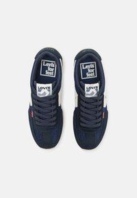 Baskets bleu marine en matériaux suédés et textiles, avec des accents blancs, un système de laçage et des étiquettes de marque sur la languette et le côté.