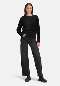 Czarny, puszysty sweter z okrągłym dekoltem i prążkowanym pasem, zestawiony z czarnymi, szerokimi spodniami z wysokim stanem oraz masywnymi czarnymi botkami.