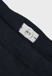 Navy geribbelde tailleband met witte binnenlabel en doorzichtige knop. Materiaal lijkt stevig en elastisch, geschikt voor een comfortabele pasvorm.