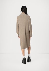 Beige knitted dress with a high collar, long sleeves, and ribbed texture, falling to mid-calf, worn with chunky black platform shoes.