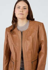 Braune Lederjacke mit einem Frontreißverschluss, zwei seitlichen Taschen und einer taillierten Passform. Texturierte Oberfläche mit Nahtdetails an den Schultern.