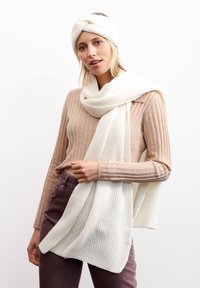Ensemble écharpe et bandeau en tricot blanc. L'écharpe est épaisse et s'enroule autour du cou, tandis que le bandeau présente un design tordu.