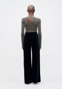 Haut en velours gris à manches longues avec un trou de serrure à l'arrière. Assorti à un pantalon en velours bleu foncé à coupe ample. Texture lisse, design simple.