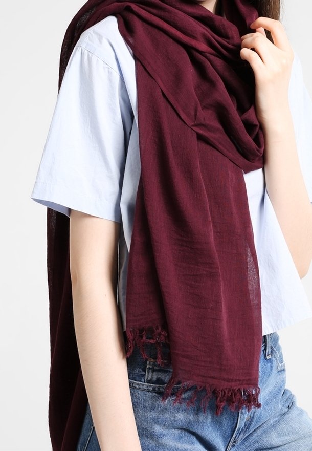 Personne portant une chemise bleu clair à manches courtes et un jean bleu, avec une grande écharpe rouge foncé drapée autour du cou et de l'épaule.