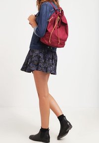 Henkilö, jolla on päällään kukallinen hame, farkkutakki, mustat nilkkurit ja punainen narureppu selässä.