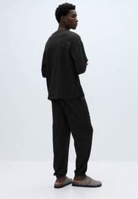 Černé tričko volnějšího střihu, odpovídající kalhoty a světle šedé nazouvací boty. Měkký materiál, jednoduchý design a pohodlné nošení.