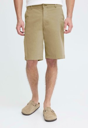 Pantalones cortos de algodón en color caqui con corte recto, bolsillos laterales y cierre de botones. Combinados con zapatos tipo mocasín de ante beige.