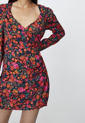 Blumenkleid mit tiefem V-Ausschnitt, auf dunklem Hintergrund mit bunten Mustern in Pink, Orange und Grün. Lange Ärmel mit Raffung.
