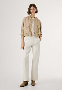 Khaki bomber jacket with two front pockets, striped top, and white wide-leg pants. Model wears brown heeled ankle boots.