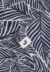 Katoenstof met een marineblauwe achtergrond en witte palmbladpatronen. Bevat een klein etiket met de letter "J".