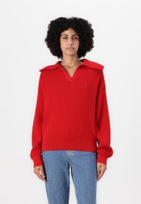 Rød strikket genser med V-hals og oversized krage, med ribbestrikkede ermer og hem, kombinert med lyseblå jeans.