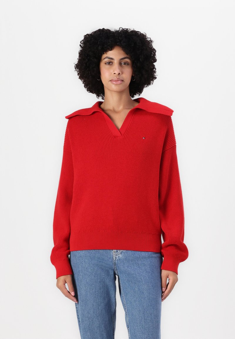Rød strikket genser med V-hals og oversized krage, med ribbestrikkede ermer og hem, kombinert med lyseblå jeans.