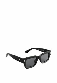 Lunettes de soleil noires à la forme rectangulaire imposante, finition mate, verres sombres et accents métalliques sur les branches.