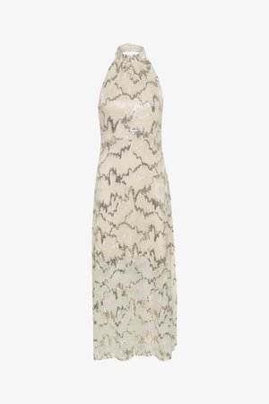 Sukienka wieczorowa na halter w jasnym odcieniu kremowym z falistym wzorem z srebrnych cekinów. Midi długości, dopasowana sylwetka i gładka tekstura.
