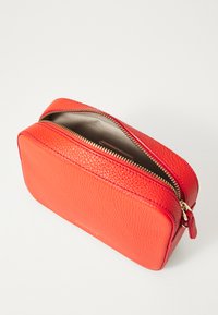 Borsa cosmetica in pelle rossa con superficie strutturata, forma rettangolare, zip dorata e interno di colore chiaro. Nota per il suo design elegante.