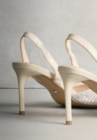 Sandaaltjes met hak, een bovenkant van crèmekleurig kunstleer, verstelbare bandjes en een glanzende, gestructureerde binnenzool. Ze hebben een slanke, lichtgekleurde hak.