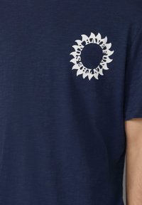 Granatowa koszulka z miękkiego materiału, z białą grafiką słonecznika na lewej stronie klatki piersiowej. Krótkie rękawy i okrągły dekolt.