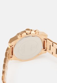 Orologio cronografo in acciaio inossidabile tono oro con fondo cassa trasparente, tre pulsanti e design a bracciale. Accenti testurizzati visibili.