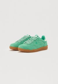 Zöld velúr sneaker, gumi talppal, textúrált felsőrésszel és egyszínű fűzőkkel. Különleges fehér díszítéssel a saroknál.